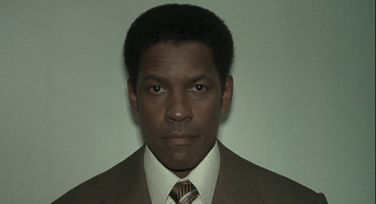 Close up shot of Denzel Washington as Frank Lucas standing in front of a pale green wall in American Gangster.